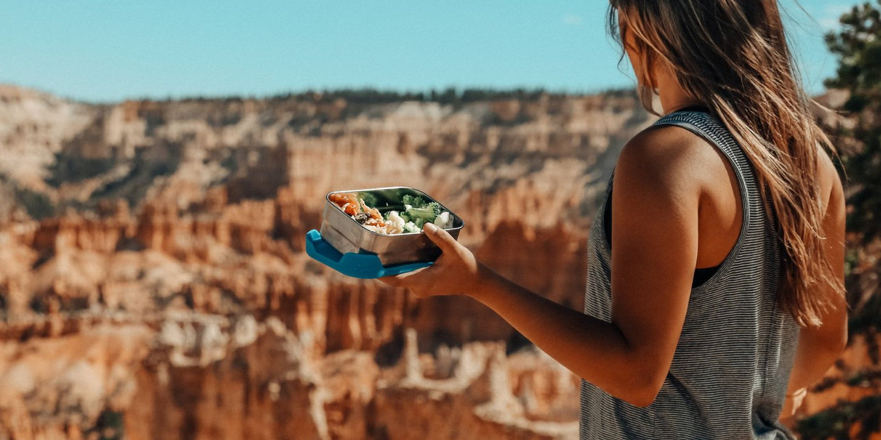 Vrouw met ECOlunchbox kijkt uit over canyon